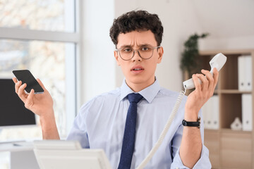 Stressed businessman with mobile phone and telephone in office