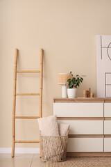 Interior of modern room with stylish dresser, basket and ladder near beige wall