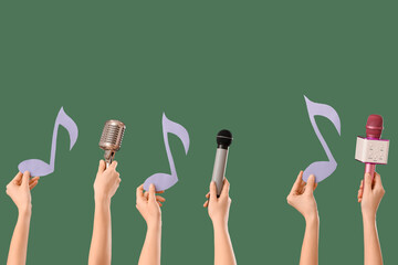 Female hands holding microphones with paper music notes on dark green background