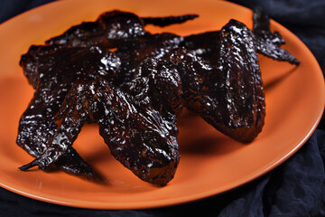 Bat wings. Cooked in sweet and sour sauce with cuttlefish ink, served with ketchup on a plate. An original idea for a Halloween party