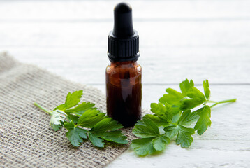 Side view of homemade herbal medicinal tincture made from parsley Petroselinum crispum. Green leaves and brown pipette bottle composition. White wood board background.