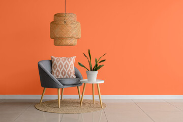 Stylish armchair and houseplant on table near orange wall in room