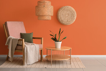 Table and armchair near orange wall in interior of living room