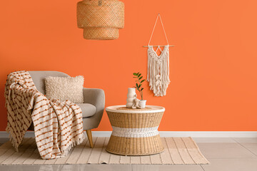 Table and comfortable armchair near orange wall in interior of living room