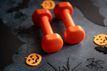 Dumbbells and Halloween pumpkins, spooky Jack-o'-lantern decorations. Healthy fitness lifestyle composition. Gym workout, sport training concept, staying in shape during autumn fall season.