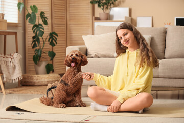 Sporty teenage girl holding Poodle dog's paw at home