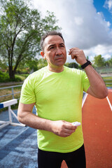 Mature athlete putting wireless earbuds before starting running on track