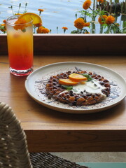 A melted vanilla ice cream and slices of an orange on top of chocolate waffle served with orange juice.