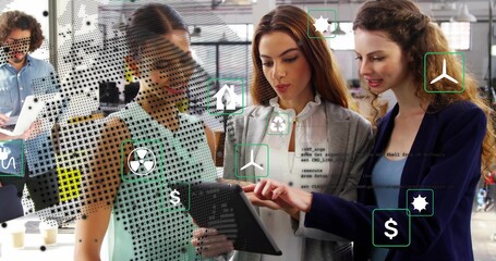 Team examining tablet in office featuring green icons, money icons, code icons, laptop, coffee cups