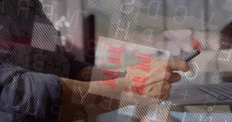 Business professional holding pen reviewing printed bar charts at office desk, with laptop overlays