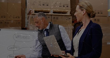 Colleagues pointing and reviewing logistics on whiteboard in warehouse, with laptop and box stacks