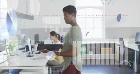 Standing office worker holding laptop in open plan office, with AR displays overlaying background