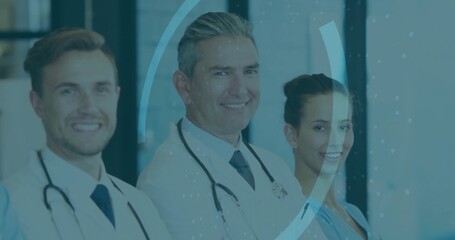 Standing medical team showcasing lab coats, stethoscopes and blue scrubs in clinic corridor