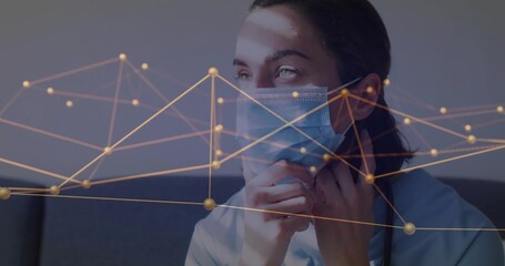 Woman in scrubs pulling mask straps downward in room, with blue mask and golden network overlay