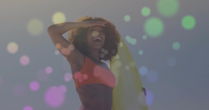 Smiling adult female surfer shielding eyes at sandy beach, showcasing yellow surfboard and bikini - Powered by Adobe