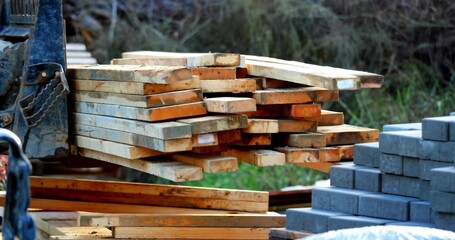 Lifting plank bundle using forklift mounting plate and chain at storage yard, with concrete blocks