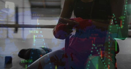 Tying female athlete winding red hand wraps around fist in gym, with barbell rack, digital overlay