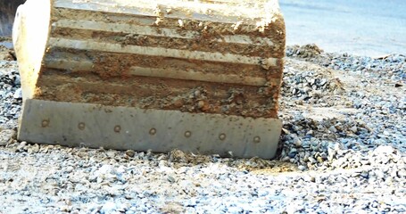 Pressing excavator bucket blade into loose gravel and pebbles on riverbank, with mud and bolt heads