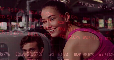 Pausing female wearing pink tank top holding cable machine handle at gym, with stock ticker overlay