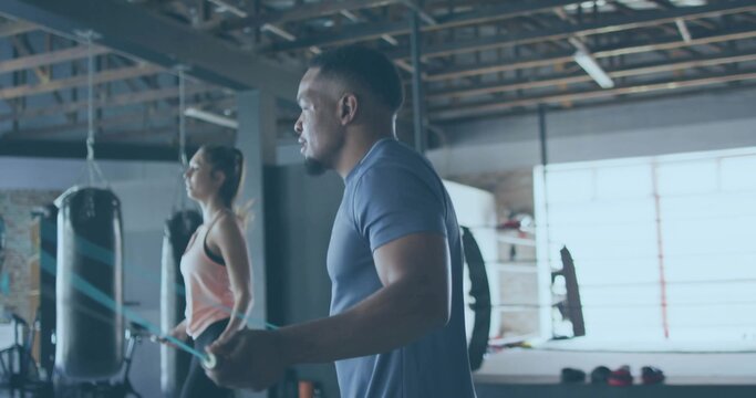 Skipping man wearing navy T-shirt and shorts holding jump rope in boxing gym, with punching bags - Powered by Adobe
