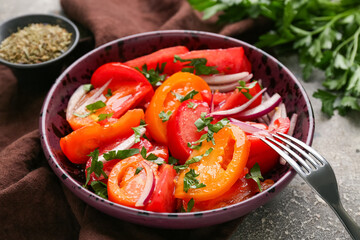 Bowl of fresh tomato salad with red onion and parsley on grey background, closeup