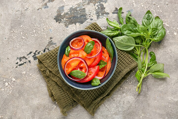 Bowl of fresh tomato salad with red onion and basil leaves on grey background