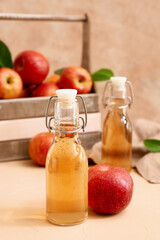 Bottles of fresh apple cider and wooden box with fruits on beige background