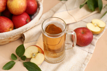 Glass cup of fresh apple cider and wicker basket with fruits on beige background