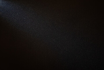 Light beam illuminating countless dust particles floating in the air against a black background,...