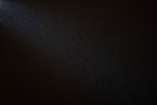 Light beam illuminating countless dust particles floating in the air against a black background, creating a mesmerizing and ethereal effect