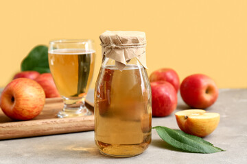 Bottle and glass of fresh apple cider with fruits on grey table