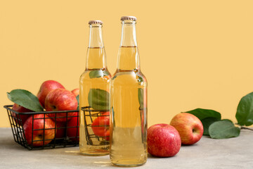 Bottles of fresh apple cider and basket with fruits on grey table