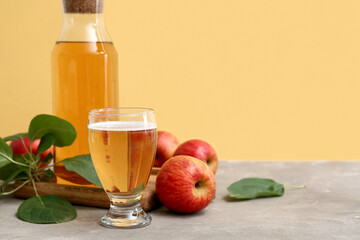 Glass and bottle of fresh apple cider with fruits on grey table