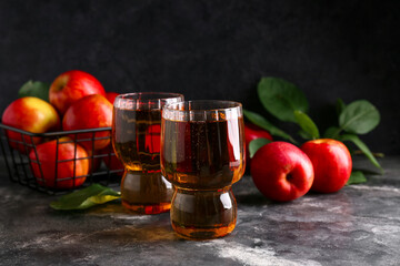 Glasses of fresh apple cider and fruits on dark background
