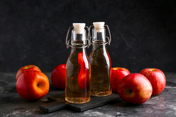 Bottles of fresh apple cider and fruits on dark background