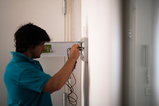 A man uses a clamp meter to check circuit breakers and the differential in an electrical panel. 