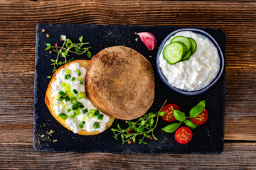 Cottage cheese roll with fresh herbs on stone board on wooden table