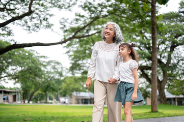 Fototapeta premium Happy old woman grandmother holding hand walking with a kid girl granddaughter in the park or garden