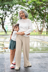 Fototapeta premium Kid girl granddaughter hugging waist of old woman grandmother standing at railing around the lake.