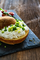Cottage cheese roll with fresh herbs on stone board on wooden table