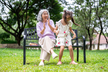 Fototapeta premium Old woman granny clapping cheering for a kid girl granddaughter dancing on grass in the park.
