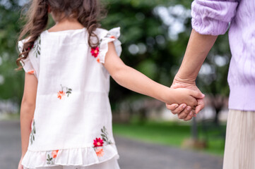 Back view old woman grandmother holding hand walking with kid girl granddaughter on sidewalk in park