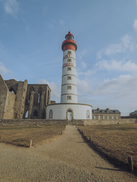 View of the striking Phare de Saint-Mathieu lighthouse, with its red top and white body, stands tall beside the weathered abbey ruins, Plougonvelin, Bretagne, France.