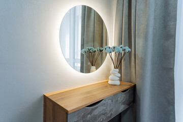 A beautifully styled vanity adorned with a round mirror is further enhanced by a charming vase of...