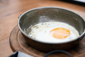 Close-Up of a Fried Egg in a Rustic Metal Pan on Wooden Table