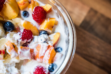 Bowl of fresh fruit salad with yogurt on wooden table surface from top view
