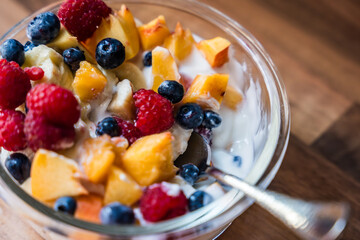 Bowl of fresh fruit salad with yogurt and spoon on wooden table surface