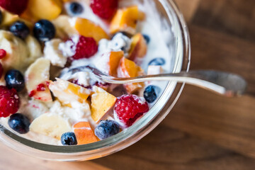 Bowl of fresh fruit salad with yogurt and spoon on wooden table surface