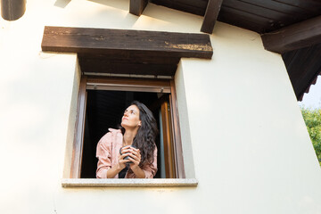 Woman enjoying morning coffee at window, looking up with hope