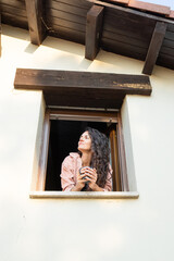 Woman enjoying morning coffee at the window of her house